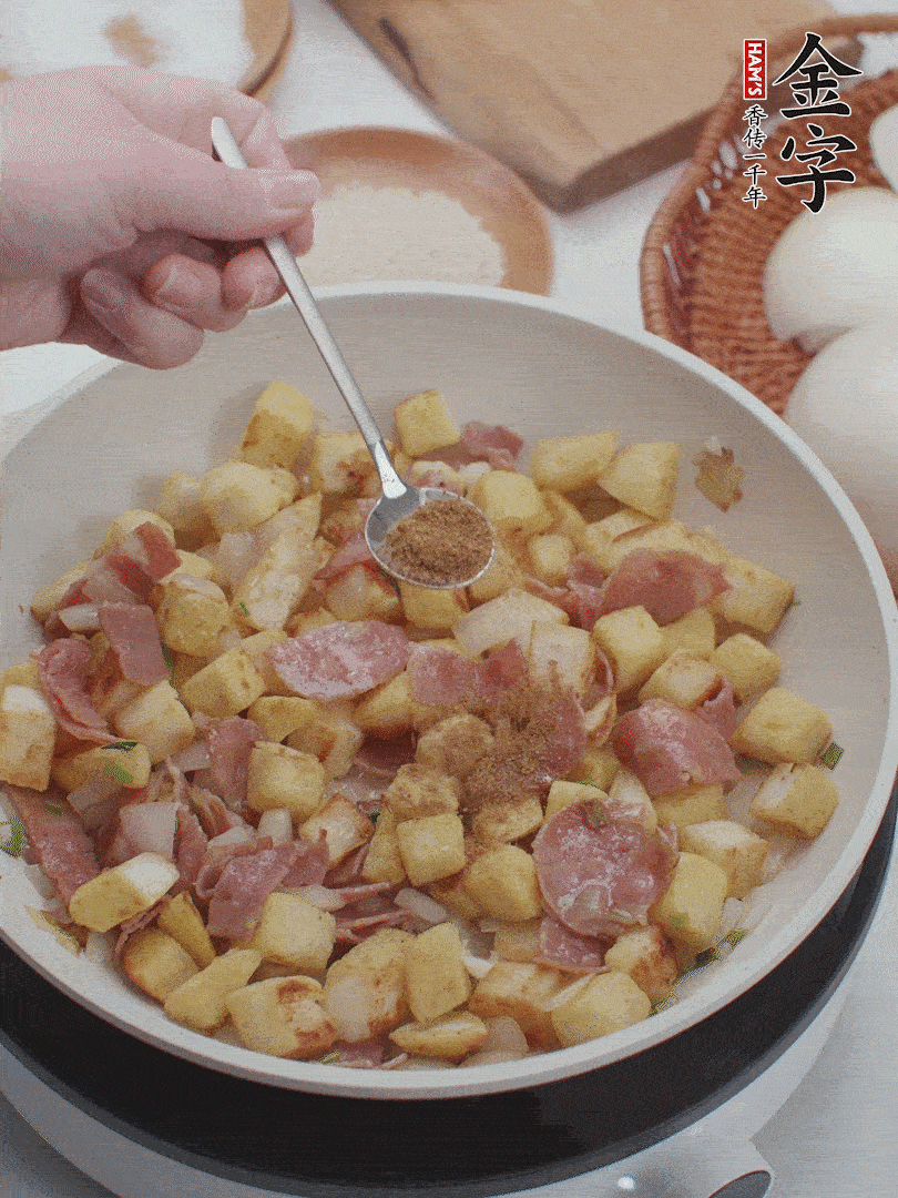 起鍋少油，煸香洋蔥丁、蔥白，加入金字培根火腿翻炒幾下，再加入饅頭丁、1小勺孜然粉、少許鹽翻炒均勻并鋪平。