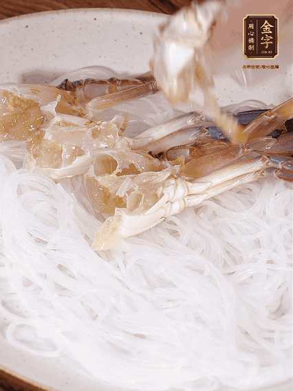 盤底墊上粉絲，擺上梭子蟹、火腿片，撒姜粒，淋上蒸魚豉油、花雕酒調(diào)味腌制15分鐘